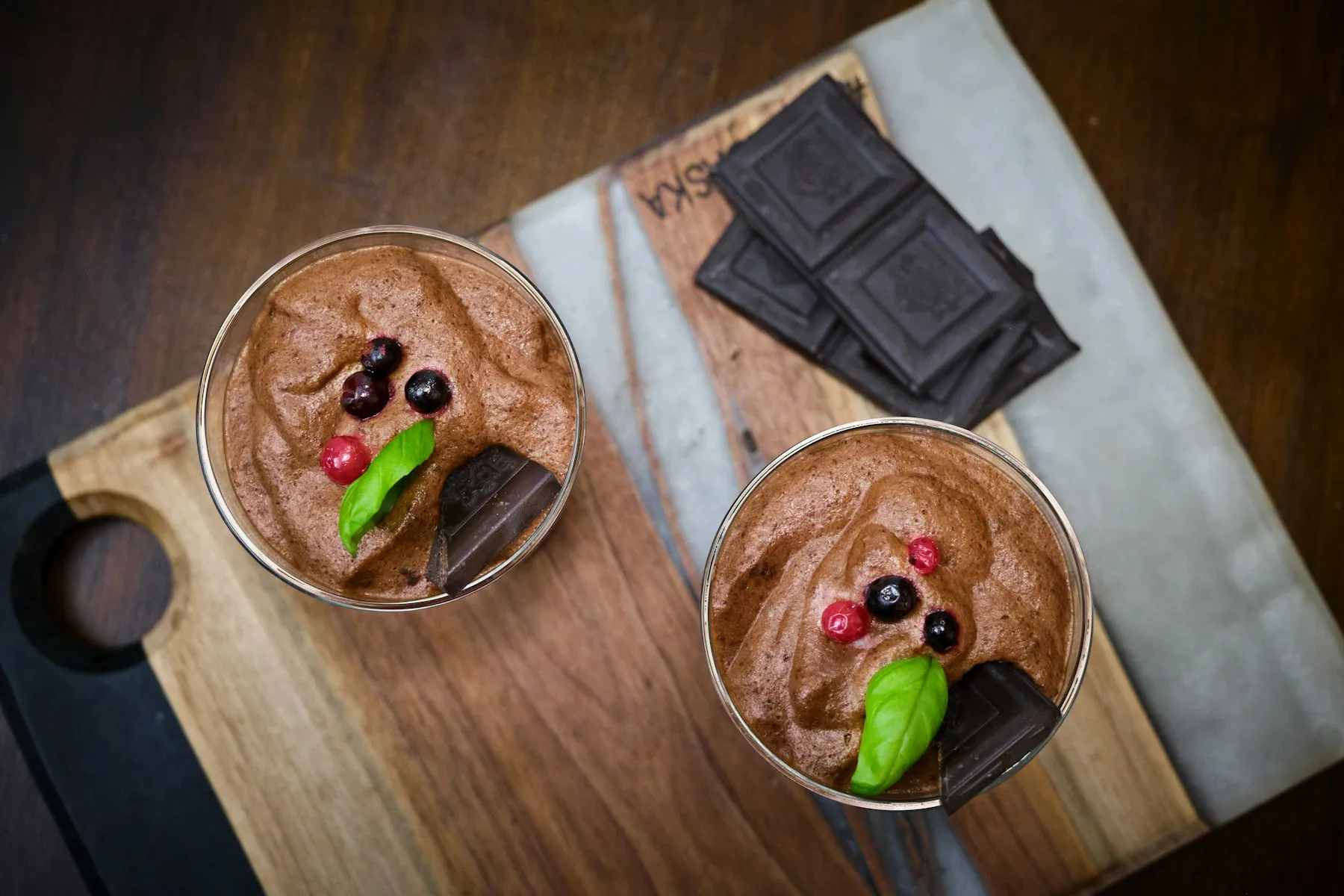 Two glasses of silky chocolate avocado mousse topped with berries, beside squares of dark chocolate