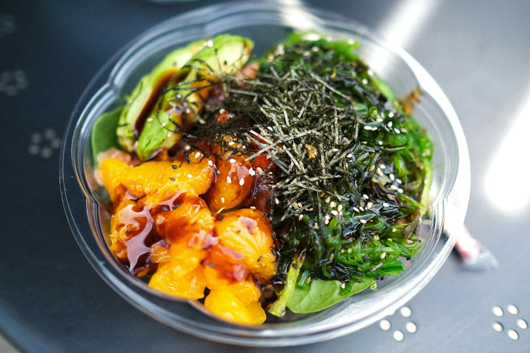 A rice bowl topped with sliced ripe avocado, salmon, seaweed, and sesame seeds