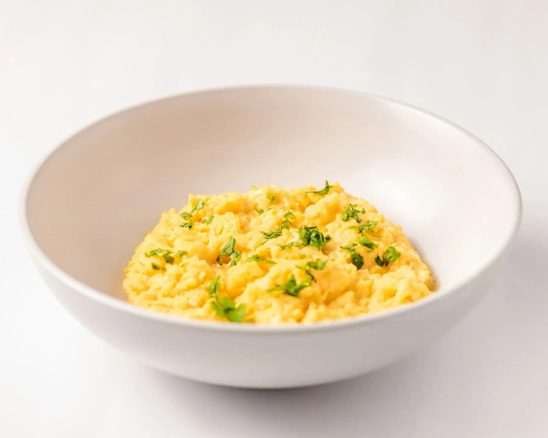 Soft golden scrambled eggs flecked with fresh herbs in a white bowl