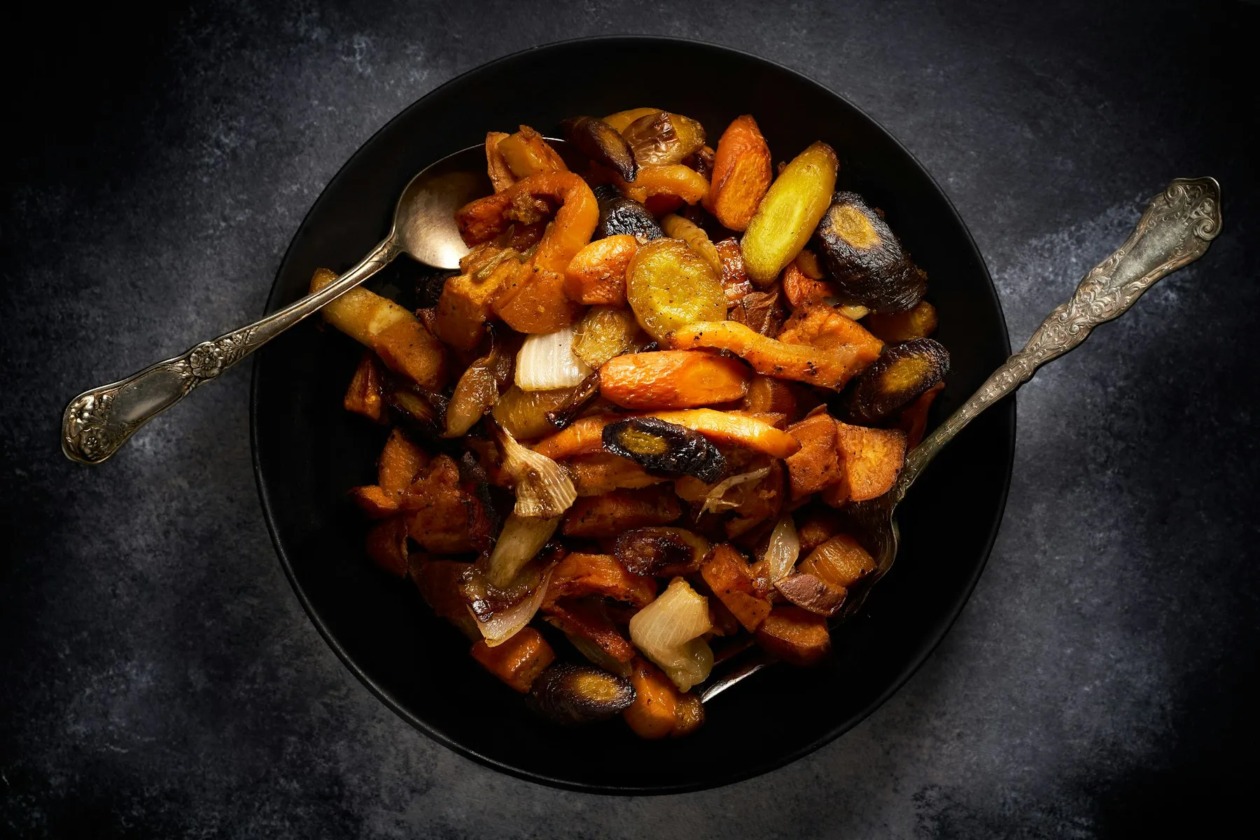 Turmeric roasted carrots and root vegetables with crisp caramelized edges in a dark bowl